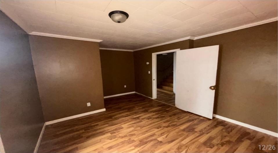 836 Mill Creek Road Troy, TN 38260 - Photo 3 of 6 Spacious room featuring wood-finish flooring, neutral brown walls, white baseboards, crown molding, and a flush-mount ceiling light fixture