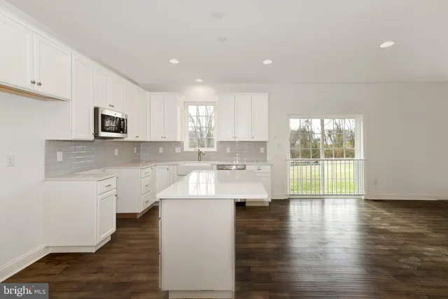 a large kitchen with stainless steel appliances granite countertop a stove a sink and white cabinets with wooden floor next to windows