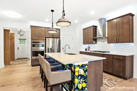 a kitchen with stainless steel appliances granite countertop a sink a stove a refrigerator a dining table and chairs with wooden floor