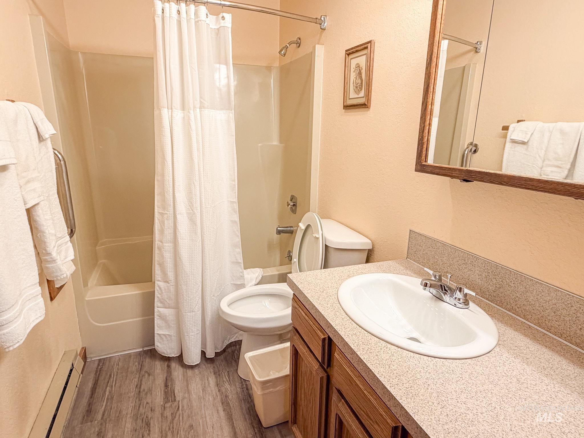 1630 Davis Avenue, Unit F46 McCall, ID 83638 - Photo 5 of 23 Bathroom featuring shower / tub combo with curtain, vanity, a baseboard heating unit, a textured wall, and dark wood-style floors