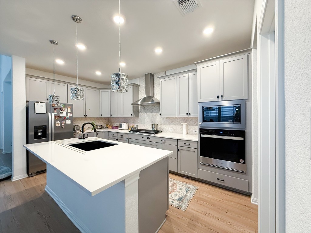 253 Inlet Lane Leander, TX 78641 - Photo 8 of 23 Kitchen with appliances with stainless steel finishes, pendant lighting, gray cabinets, a center island with sink, and wall chimney range hood