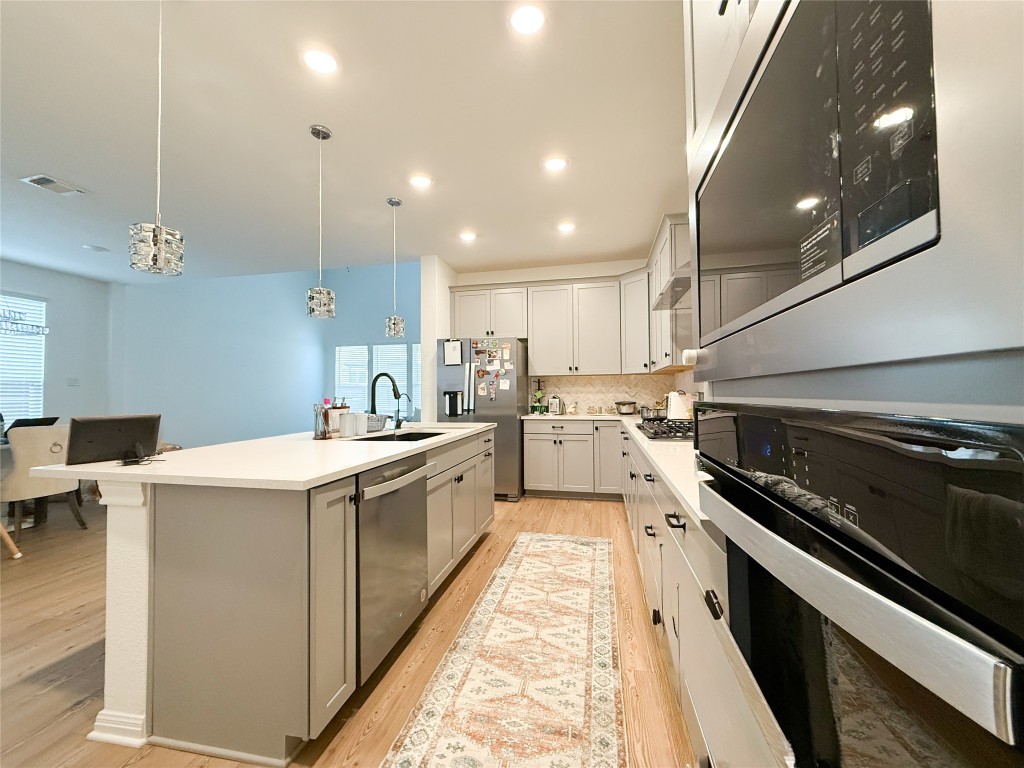 253 Inlet Lane Leander, TX 78641 - Photo 9 of 23 Kitchen featuring appliances with stainless steel finishes, pendant lighting, a kitchen island with sink, light wood-style floors, and backsplash