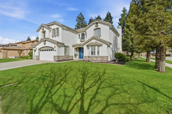 a view of white house with a big yard and large trees