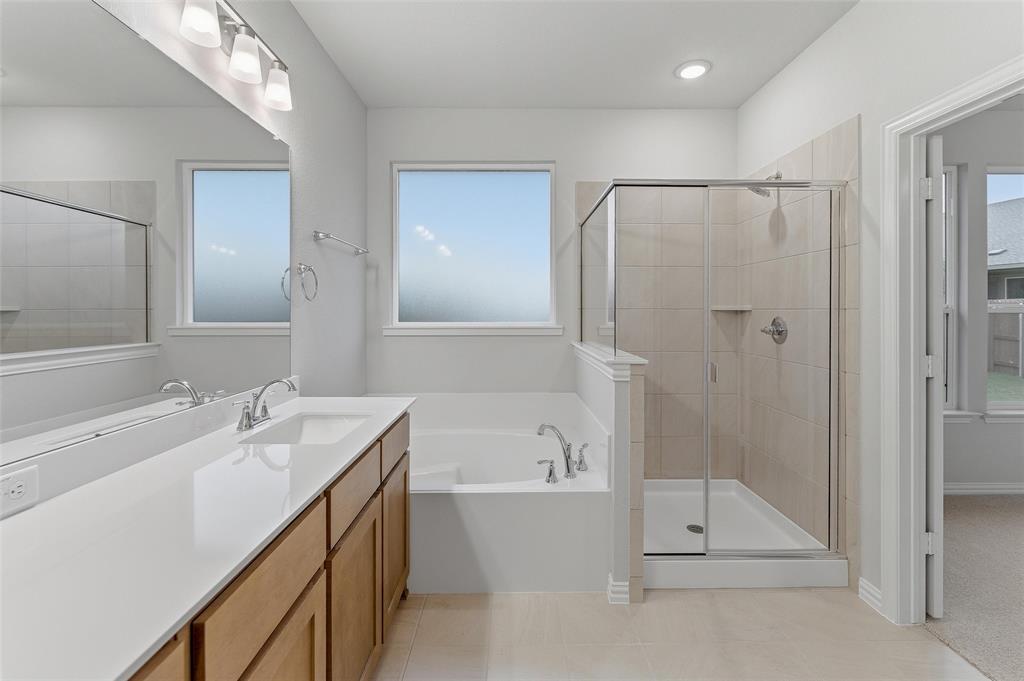 1237 Frio Drive Springtown, TX 76082 - Photo 18 of 25 Bathroom featuring a double vanity with light wood-finish cabinetry, a large integrated mirror, an undermount soaking tub, a tiled walk-in shower with a glass enclosure, and two windows