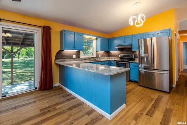 a kitchen with stainless steel appliances granite countertop a refrigerator a sink dishwasher a stove and a dining table with wooden floor