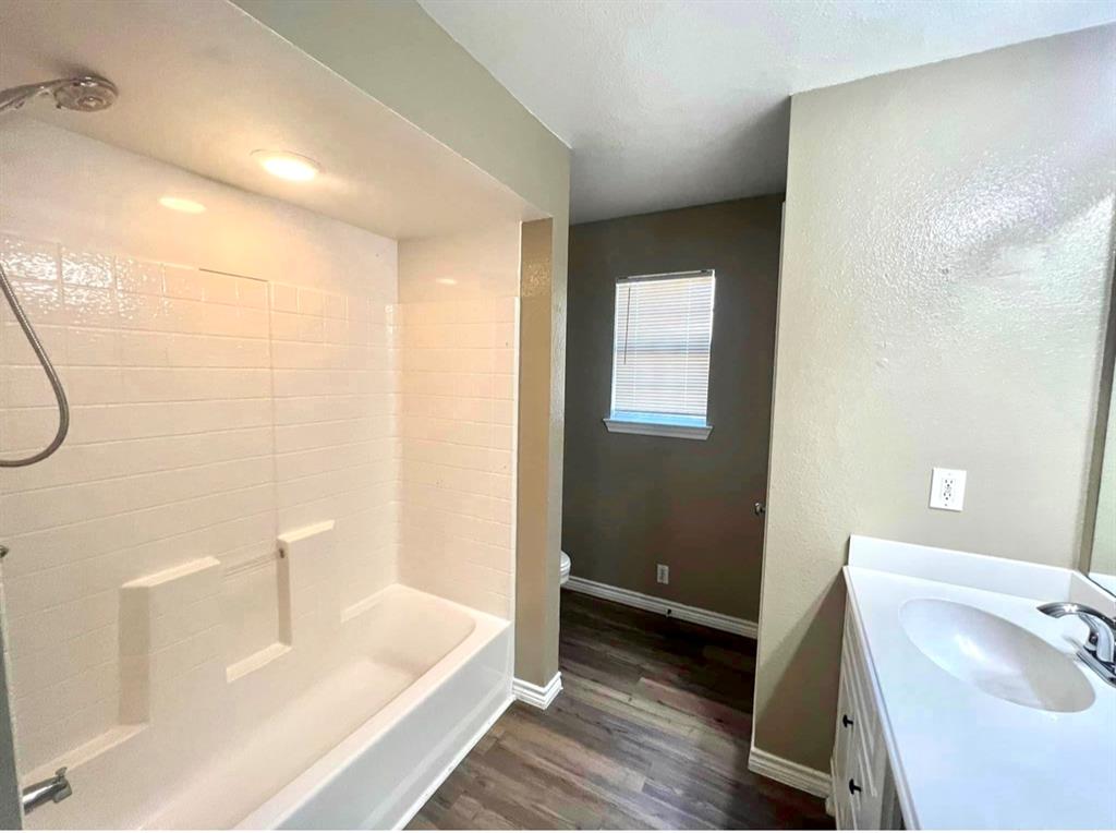 3133 Tbd County Road Lone Oak, TX 75453 - Photo 19 of 21 Bathroom featuring a white bathtub with subway tile surround, recessed lighting, wood-finish flooring, a white vanity with an integrated sink, and a window with blinds