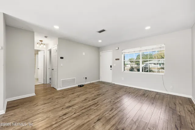 a view of an empty room with wooden floor and a window