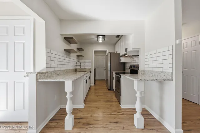 a kitchen with stainless steel appliances kitchen island granite countertop a refrigerator a stove and white cabinets with wooden floor