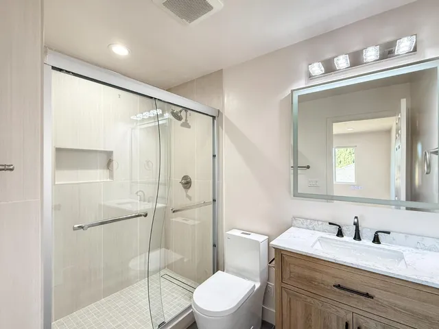 a bathroom with a granite countertop sink toilet a mirror a vanity and shower
