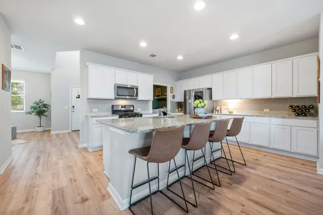a kitchen with stainless steel appliances granite countertop a refrigerator a stove top oven a sink dishwasher and white cabinets with wooden floor
