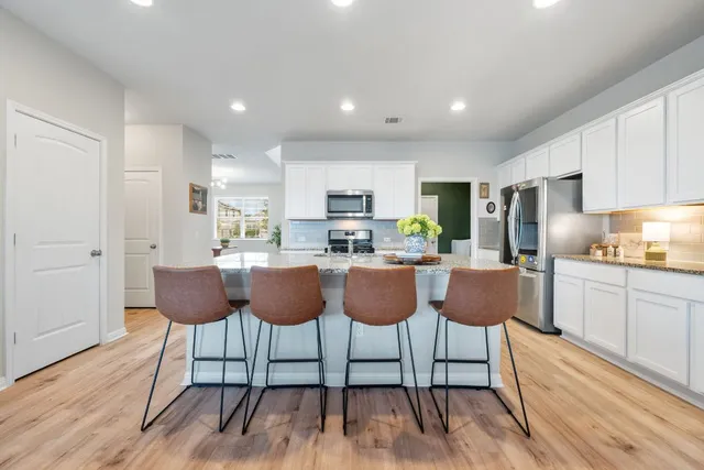 a kitchen with granite countertop a dining table chairs cabinets wooden floor and stainless steel appliances