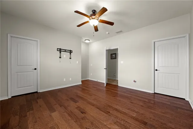 an empty room with wooden floor and a ceiling fan