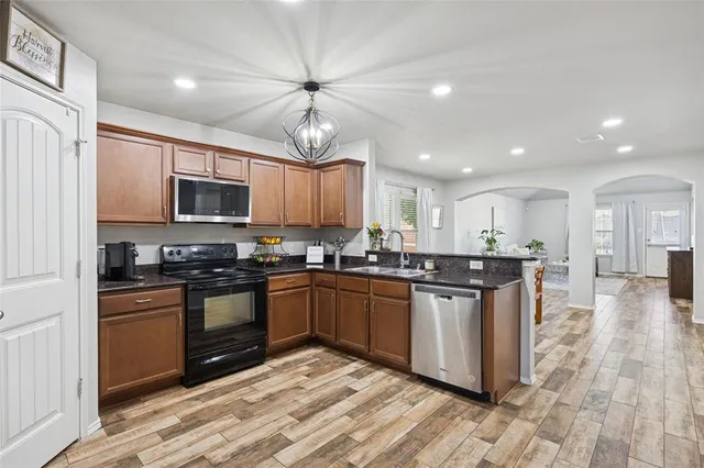 a kitchen with stainless steel appliances granite countertop a stove top oven a sink dishwasher a refrigerator and white cabinets with wooden floor