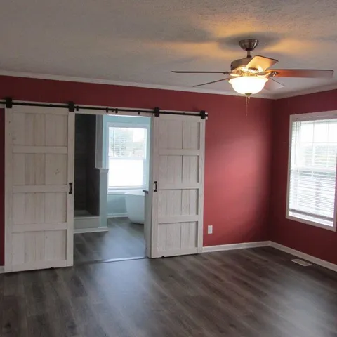 an empty room with wooden floor chandelier fan and windows