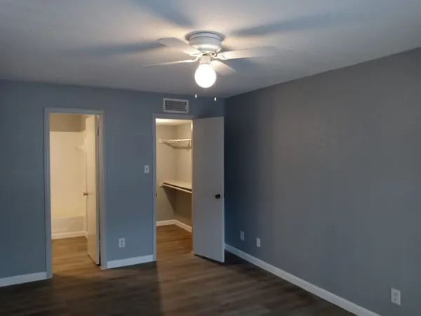 a view of an empty room with wooden floor and a ceiling fan