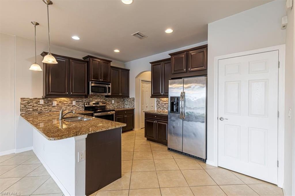 15389 Summit Pl Circle, Unit 286 Naples, FL 34119 - Photo 11 of 29 Kitchen with arched walkways, stainless steel appliances, dark wood finish cabinetry, dark stone counters, and a peninsula