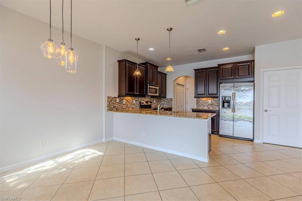 15389 Summit Pl Circle, Unit 286 Naples, FL 34119 - Photo 12 of 29 Kitchen with arched walkways, dark wood finish cabinets, stainless steel appliances, light stone counters, and pendant lighting