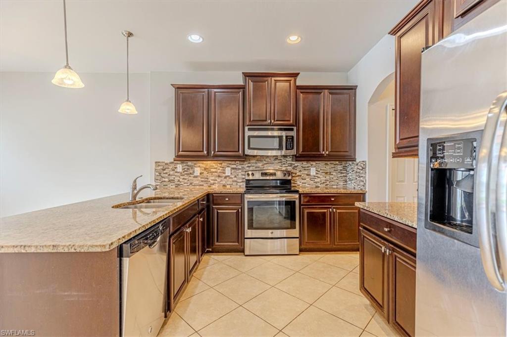 15389 Summit Pl Circle, Unit 286 Naples, FL 34119 - Photo 8 of 29 Kitchen featuring stainless steel appliances, light stone counters, decorative light fixtures, a peninsula, and decorative backsplash