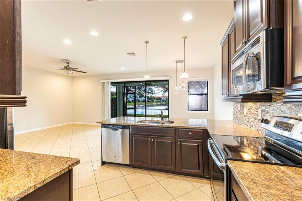 15389 Summit Pl Circle, Unit 286 Naples, FL 34119 - Photo 9 of 29 Kitchen featuring stainless steel appliances, dark wood finish cabinetry, and light stone counters