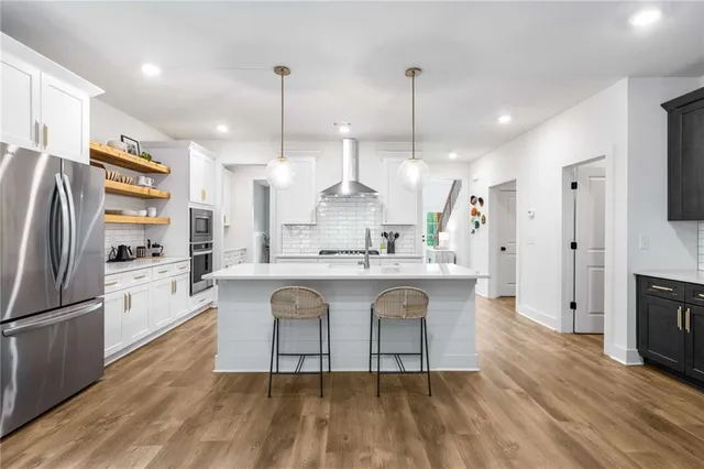 a kitchen with stainless steel appliances granite countertop a refrigerator a stove a sink dishwasher a oven and a dining table with wooden floor