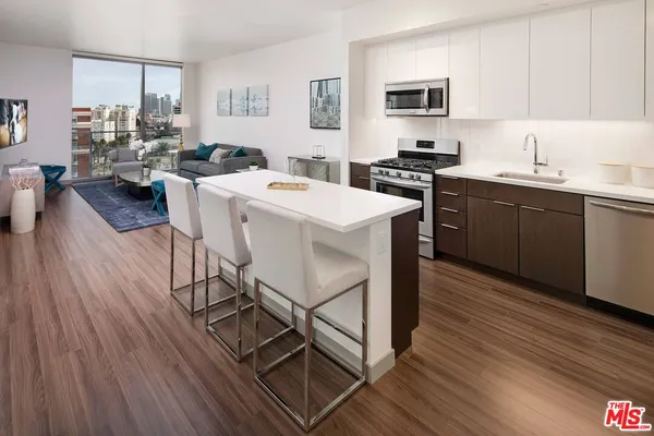 a kitchen with stainless steel appliances kitchen island granite countertop a sink dishwasher a stove a dining table and chairs with wooden floor