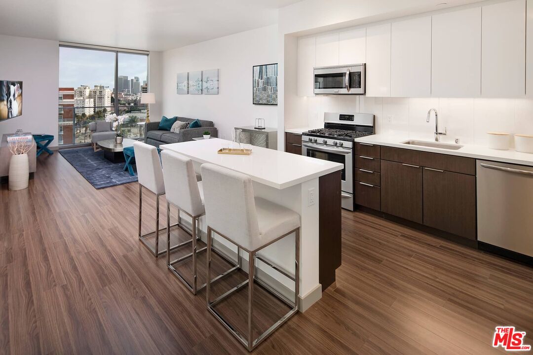 3033 Wilshire Boulevard, Unit 1707 Los Angeles, CA 90020 - Photo 16 of 32 a kitchen with stainless steel appliances kitchen island granite countertop a sink dishwasher a stove a dining table and chairs with wooden floor