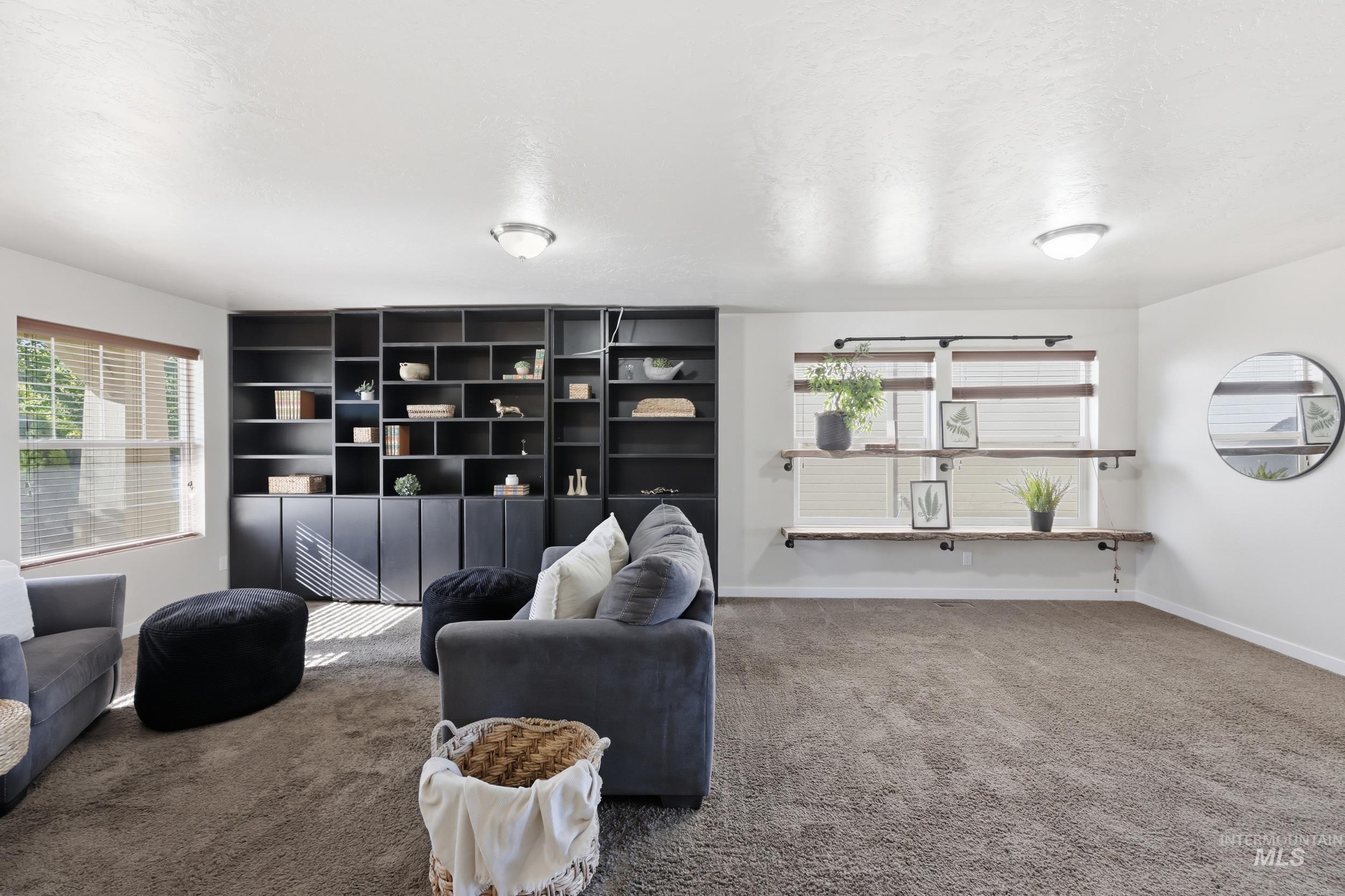 4855 South Chex Way Boise, ID 83709 - Photo 9 of 47 Spacious interior room featuring a large built-in black shelving unit with closed lower cabinetry, two windows with blinds, built-in wooden shelving below one window, and neutral-toned carpeting