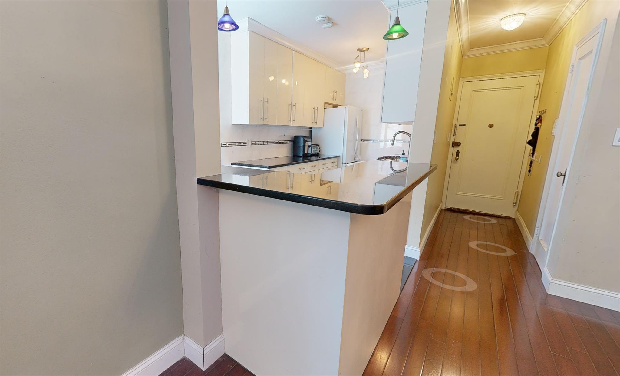 94-10 64th Road, Unit B6 Queens, NY 11374 - Photo 5 of 17 Kitchen featuring freestanding refrigerator, dark wood-style flooring, crown molding, white cabinetry, and dark countertops