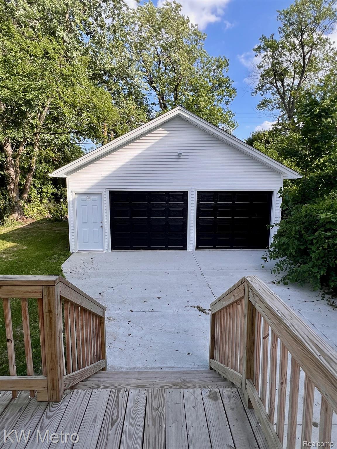 939 Webb Street Detroit, MI 48202 - Photo 18 of 19 Two-car detached garage featuring white siding, black garage doors, and a side entry door
