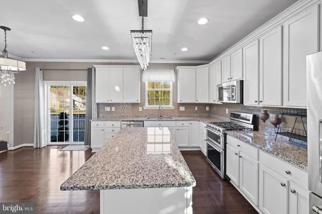 a kitchen with stainless steel appliances granite countertop wooden cabinets a sink a stove a dining table and chairs