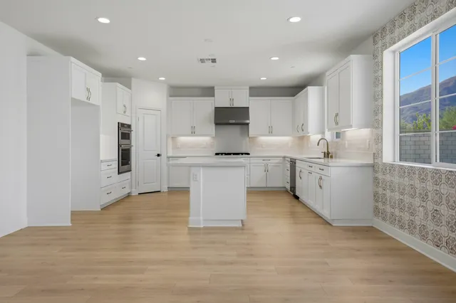 a large white kitchen with granite countertop a stove top oven a sink and a refrigerator