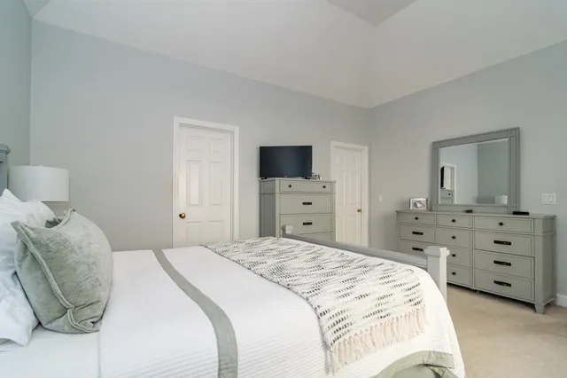 a spacious bedroom with a bed and a flat tv screen on the dresser