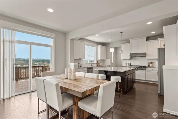 a dining hall with stainless steel appliances granite countertop a stove a refrigerator a kitchen island a couches and chairs with wooden floor