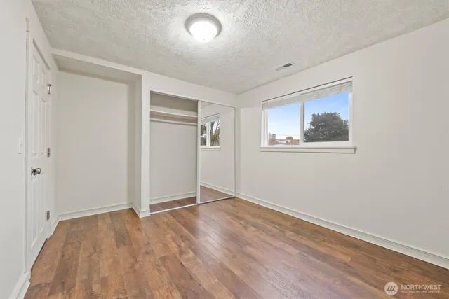 an empty room with wooden floor closet and windows