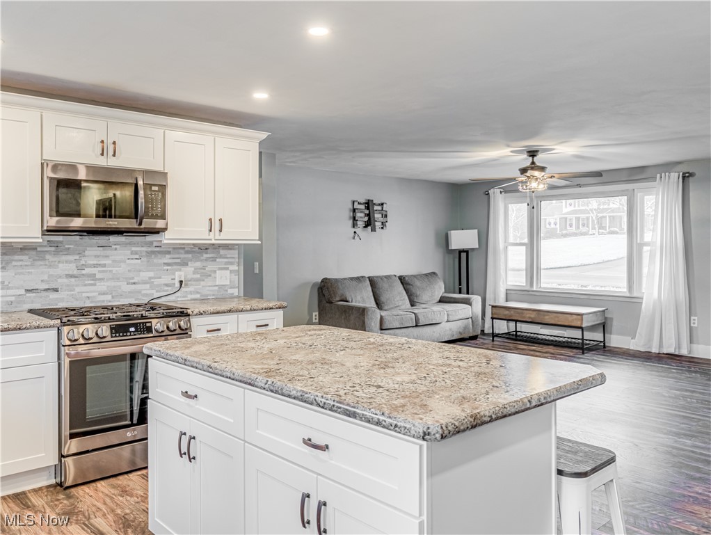 Kitchen featuring backsplash, white cabinets, light hardwood / wood-style flooring, ceiling fan, and stainless steel appliances