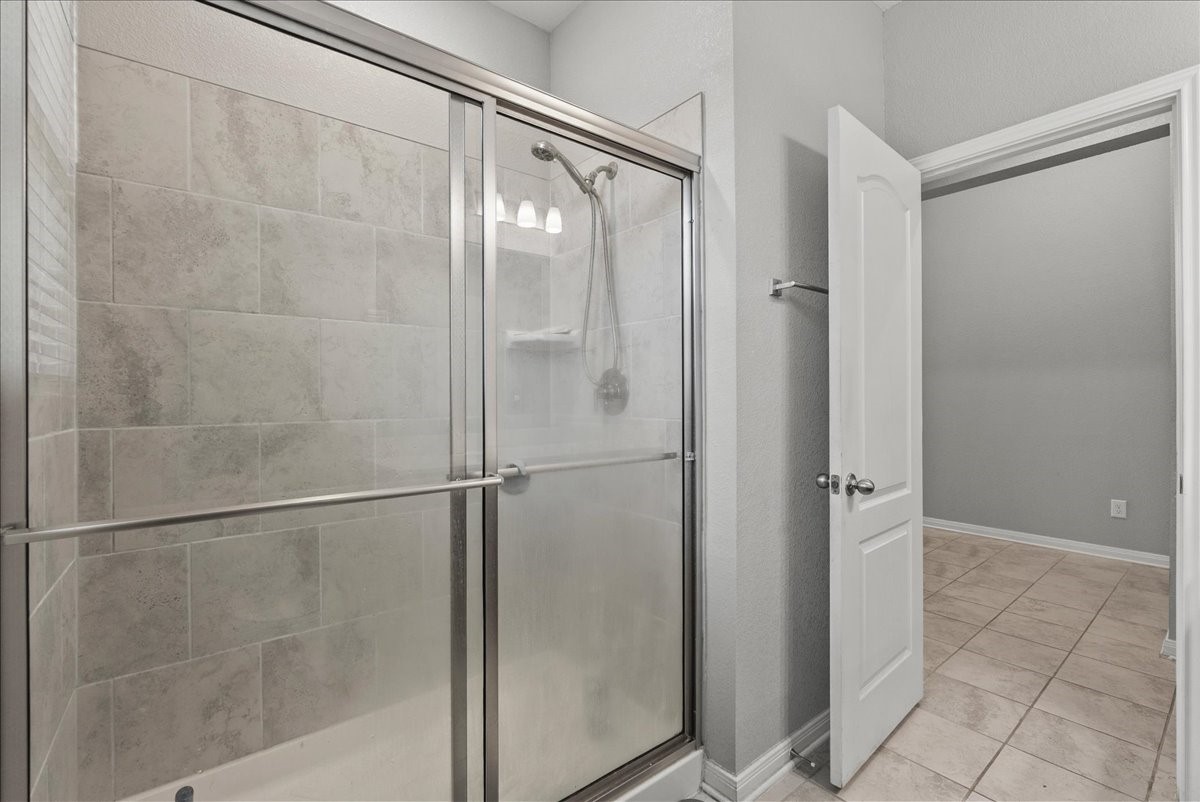 2320 Rosemary Street Rosenberg, TX 77469 - Photo 32 of 40 This photo showcases a modern bathroom with a glass-enclosed shower featuring large, neutral-toned tiles. The room is well-lit, and there's a door leading to a tiled hallway or adjacent room.