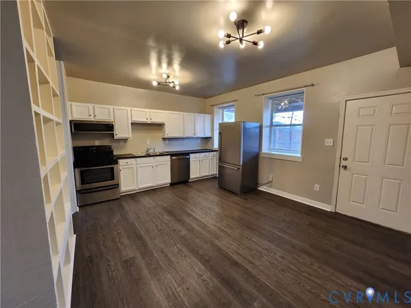 an empty room with wooden floor chandelier and windows