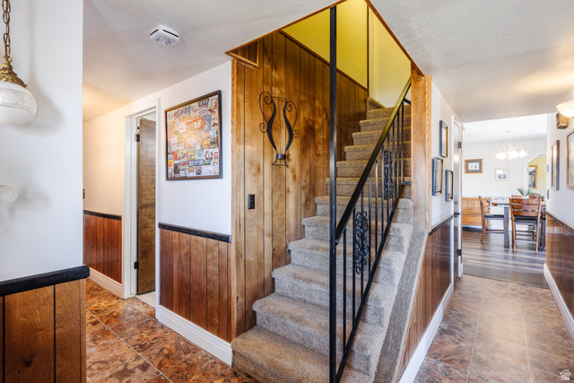 1470 Redwood Tree Street St. George, UT 84790 - Photo 28 of 53 Carpeted staircase with an ornate wrought iron railing, wood-finish wall paneling, tile flooring, and overhead lighting