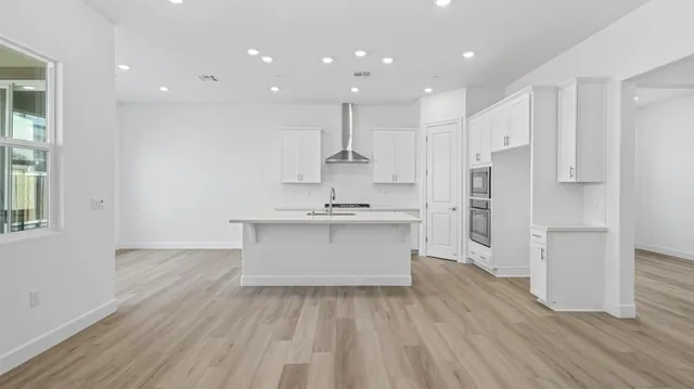 a large white kitchen with a refrigerator a sink dishwasher a stove and white cabinets with wooden floor