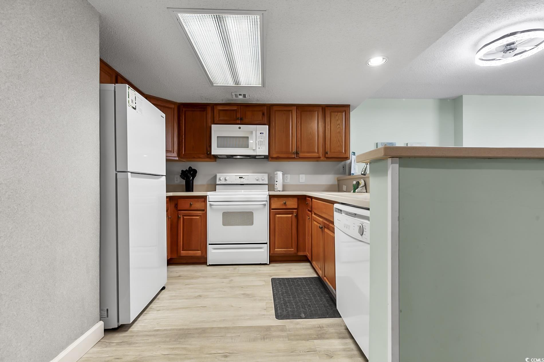 205 74th Avenue North, Unit 708 Myrtle Beach, SC 29572 - Photo 10 of 38 Kitchen featuring white appliances, light countertops, brown cabinets, light wood finished floors, and a peninsula