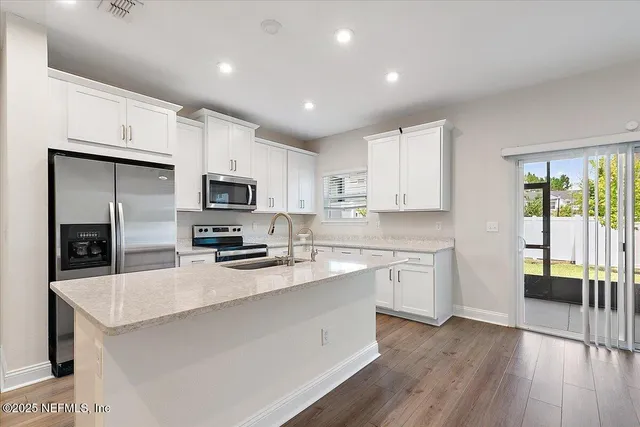 a kitchen with granite countertop a refrigerator a sink dishwasher a stove and white cabinets with wooden floor