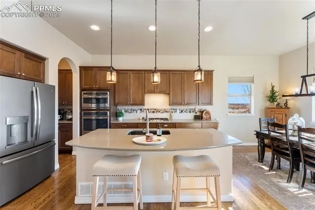 a kitchen with stainless steel appliances kitchen island granite countertop a dining table chairs and refrigerator