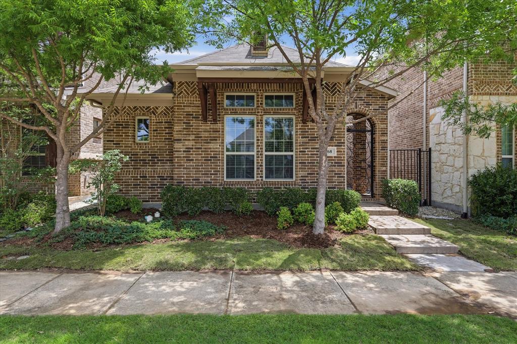 Charming brick cottage-style curb appeal framed by mature trees, manicured landscaping, and an inviting stone walkway leading to a beautifully detailed arched entry.