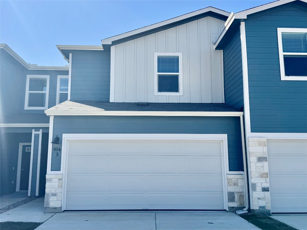 View of front facade featuring a garage, concrete driveway, board and batten siding, a shingled roof, and stone siding