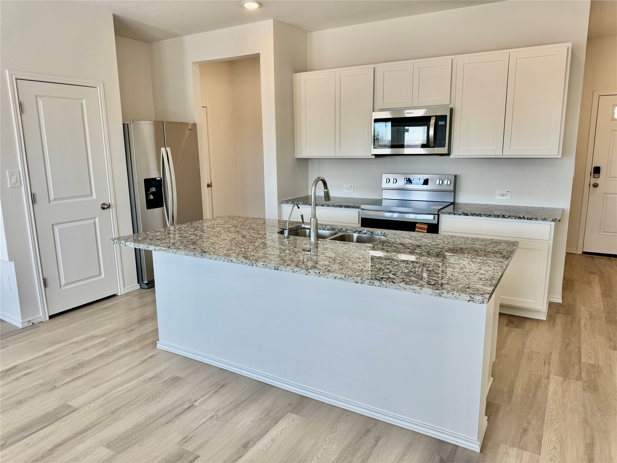 104 Calcite Road, Unit 3 Kyle, TX 78640 - Photo 2 of 7 Kitchen featuring appliances with stainless steel finishes, white cabinetry, light stone countertops, a kitchen island with sink, and light wood-style flooring