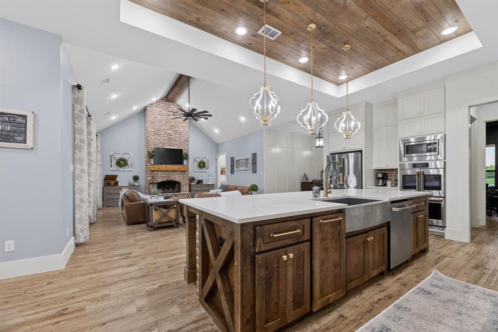 985 Vest Lane Pilot Point, TX 76258 - Photo 27 of 40 Gourmet kitchen with a wood-plank ceiling, three decorative pendant lights, stainless steel appliances, and a central island featuring a farmhouse-style sink and quartz countertop