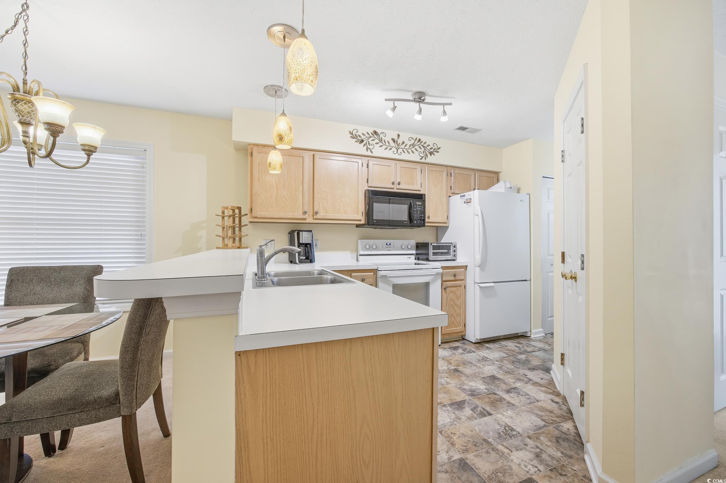 615 Tupelo Lane, Unit F Longs, SC 29568 - Photo 4 of 27 Kitchen with a peninsula, light countertops, white appliances, hanging light fixtures, and a breakfast bar area