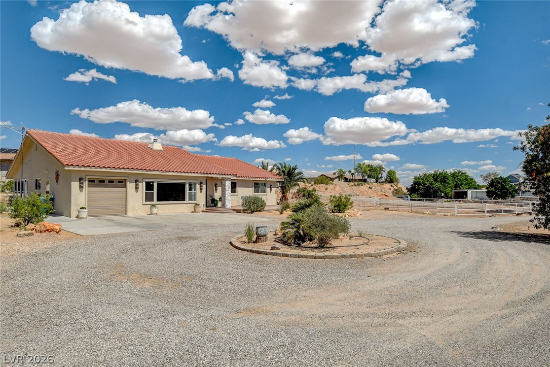 1950 Bowman Road Logandale, NV 89021 - Photo 2 of 81 A spacious gravel driveway encircles a landscaped island, leading to a charming desert home with a garage.