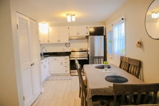 a kitchen with stainless steel appliances kitchen island granite countertop a dining table chairs and a refrigerator