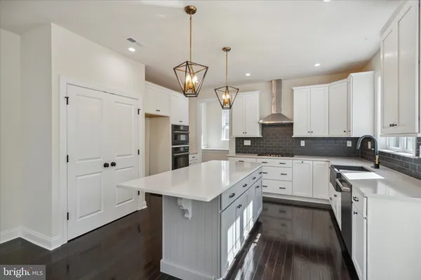 a kitchen with stainless steel appliances kitchen island granite countertop a refrigerator a oven a stove and white cabinets with wooden floor
